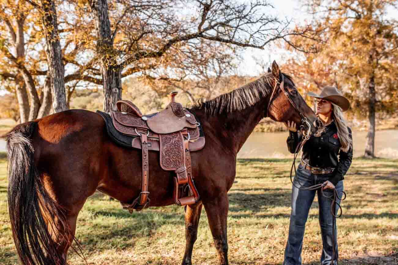 A cowgirl with her horse using a western saddle with floral carving